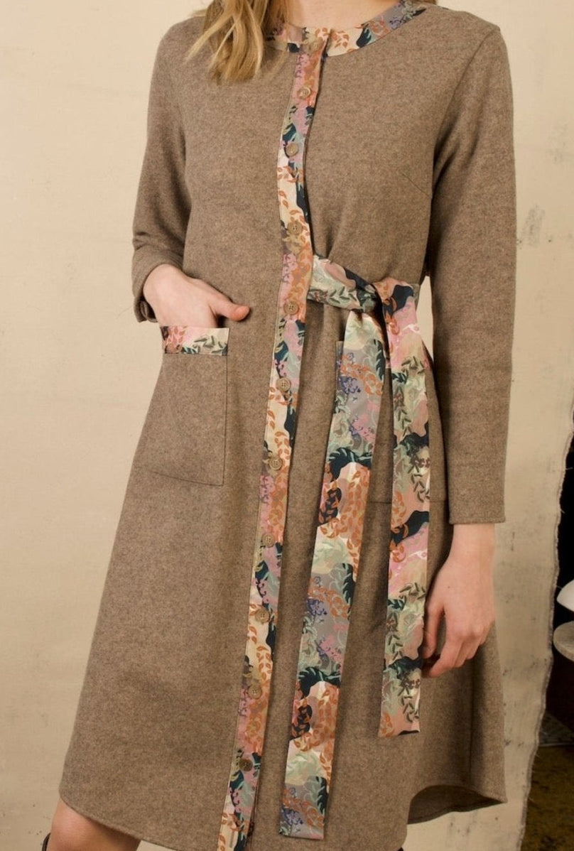 Close-up of the NNA Abigale dress showing textured taupe wool-blend fabric, printed button placket, tie belt and front patch pocket.