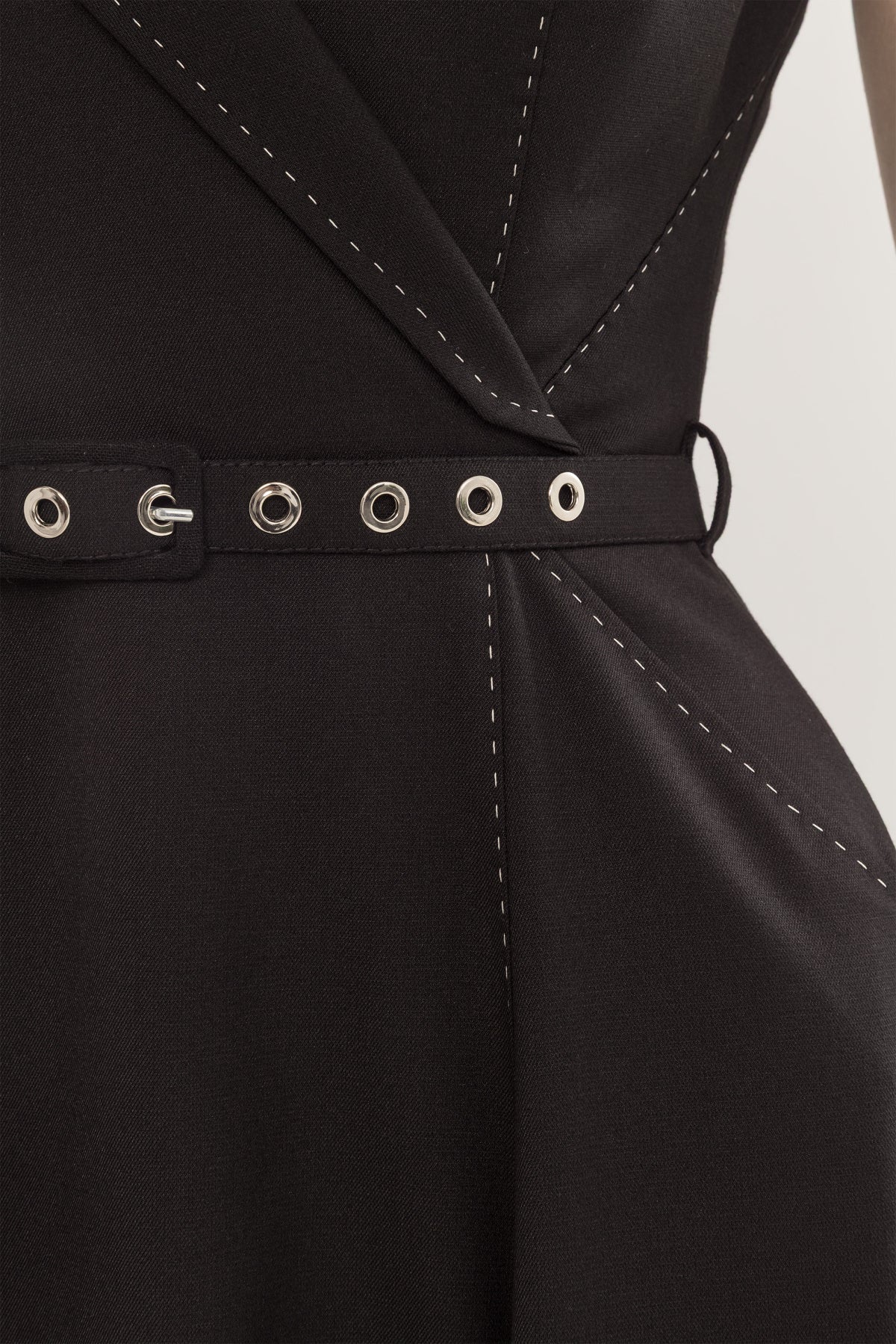 Close-up of black fabric belt with silver eyelet detail on a black A-line midi dress