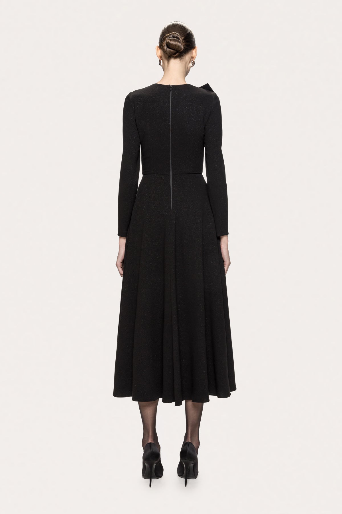 Side view of NISSA black bow midi dress showing the fitted waist, long sleeves and full skirt.
