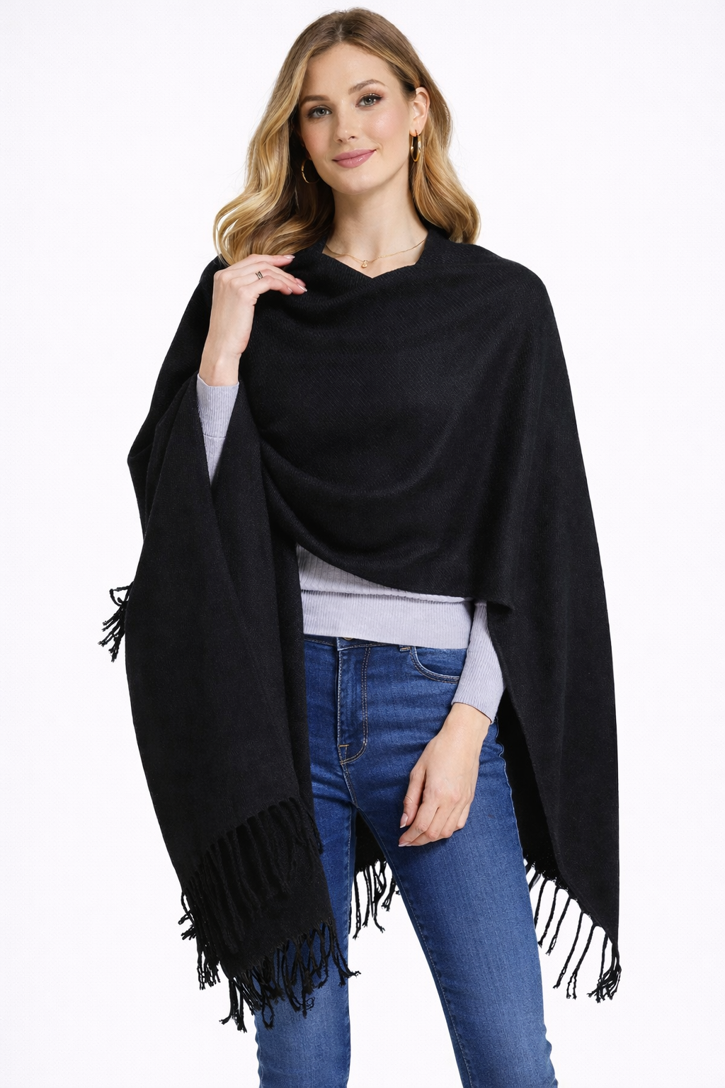 Woman wearing a black fringe poncho shawl over a gray top and blue jeans.