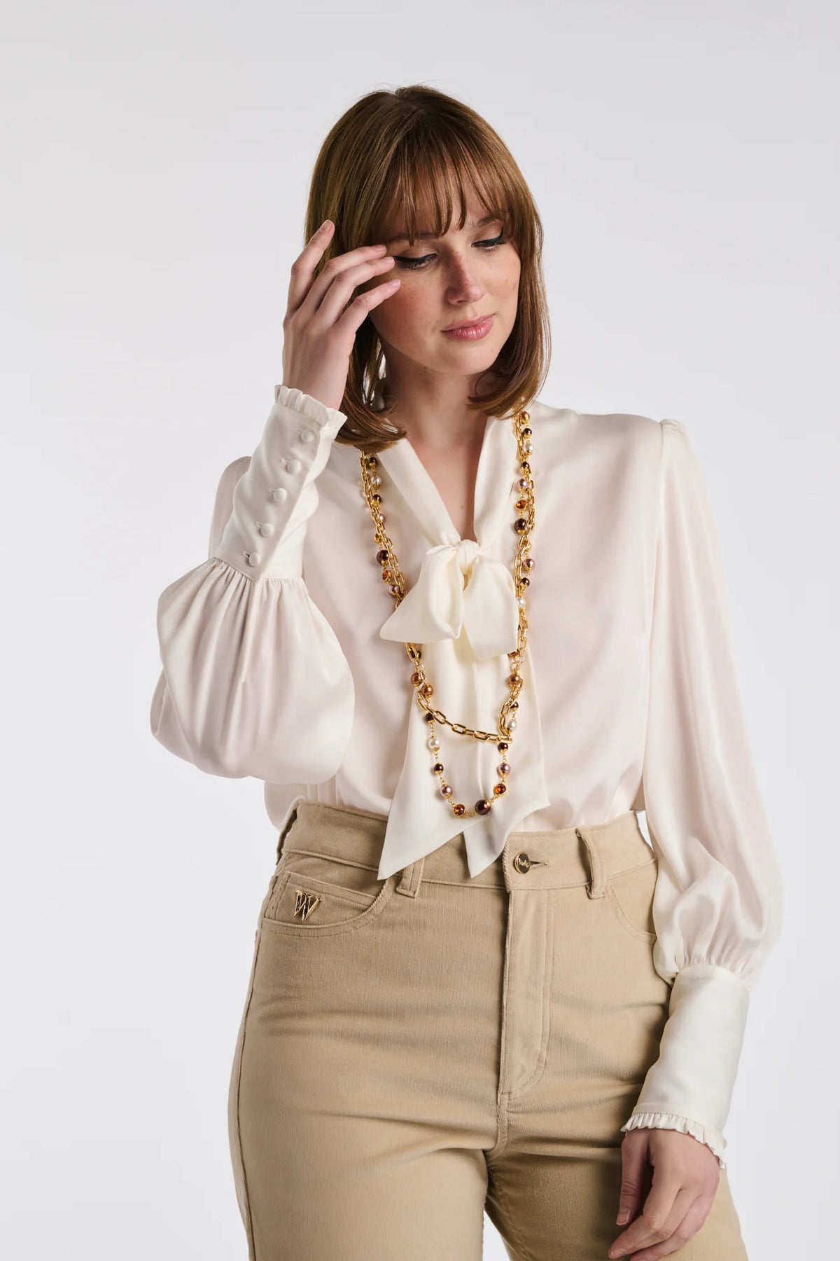 WEILL Paris gold-tone double chain necklace with brown and ivory pearl-look beads, worn over an ivory bow blouse.