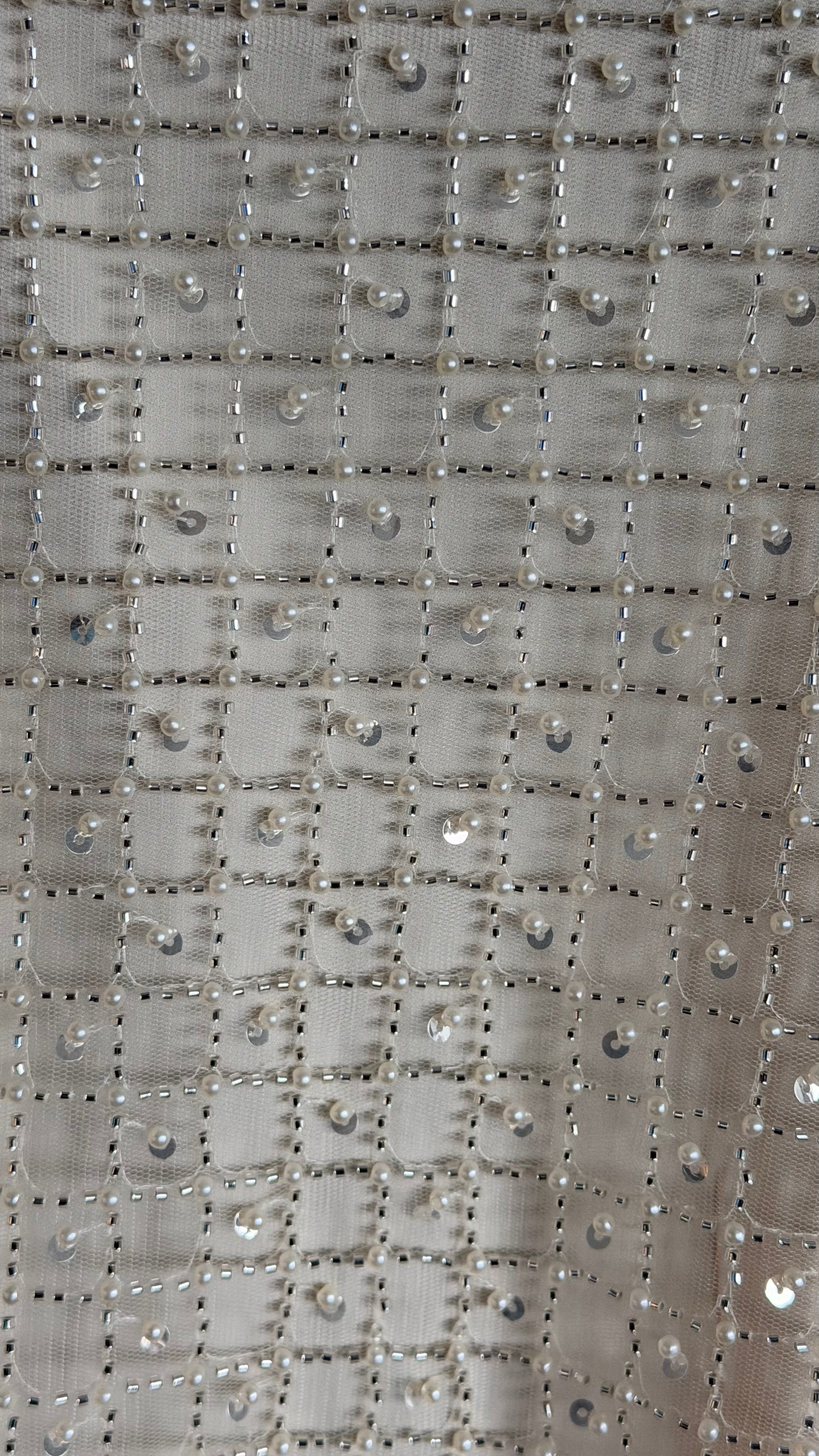 Close-up of a textured fabric with a grid pattern and small embellishments.