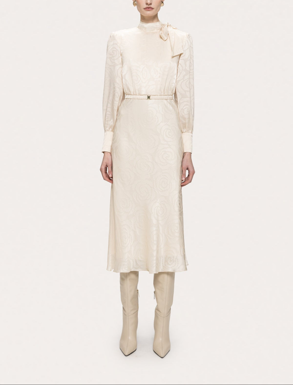 Full front view of NISSA cream satin bow-neck midi dress with a slim belt, styled with cream knee-high boots.