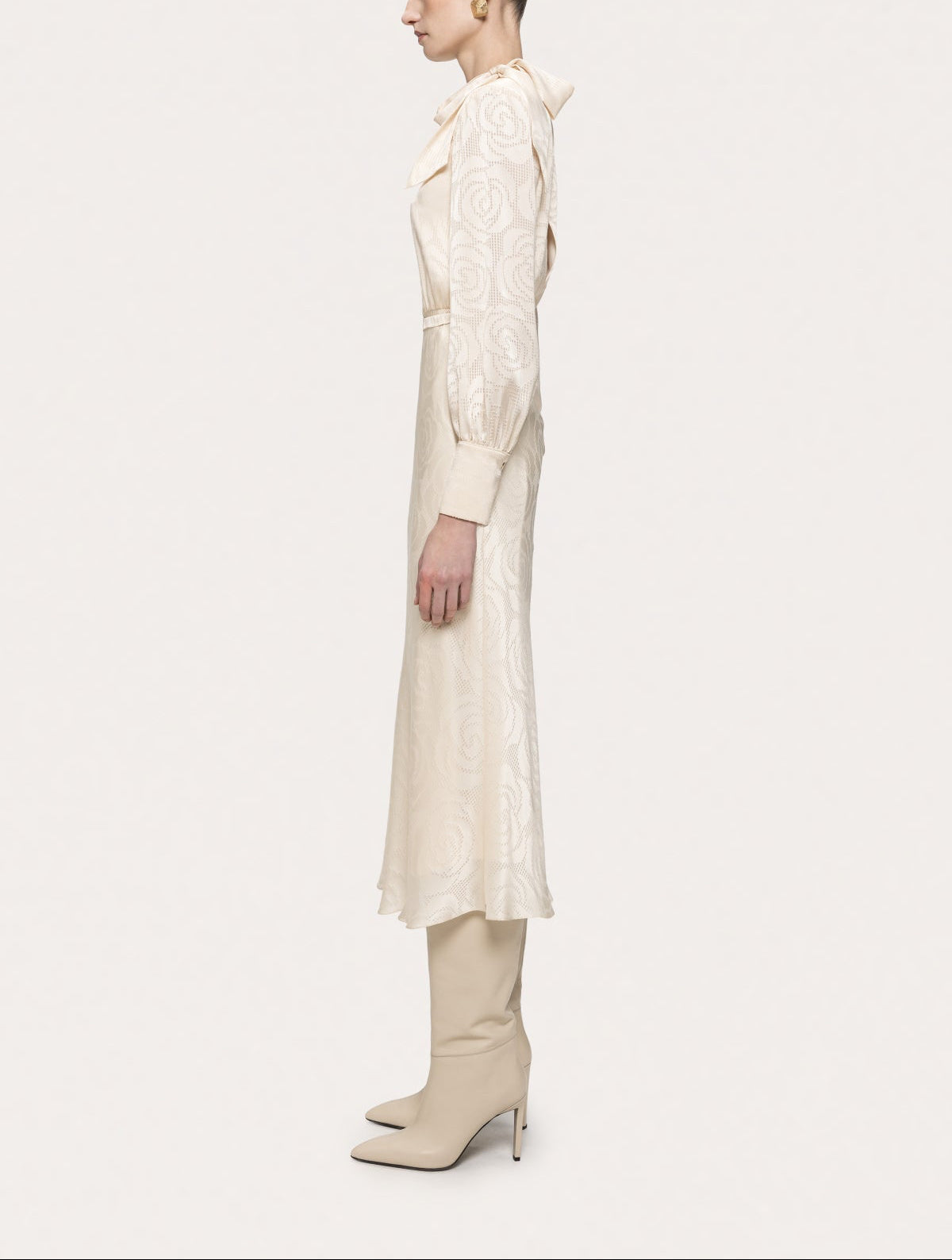 Side view of NISSA cream satin midi dress showing the shoulder bow, cuffed sleeves and gently flared skirt.