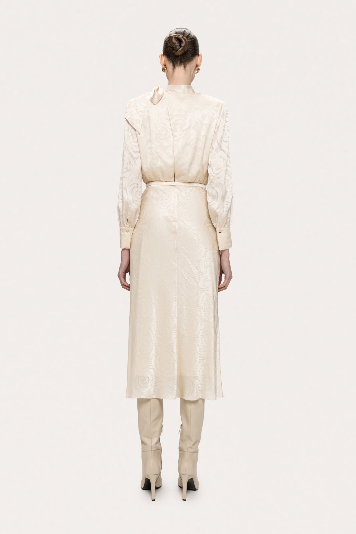 Back view of NISSA cream satin midi dress with a high closed back, back zipper, slim belt and long button-cuff sleeves.