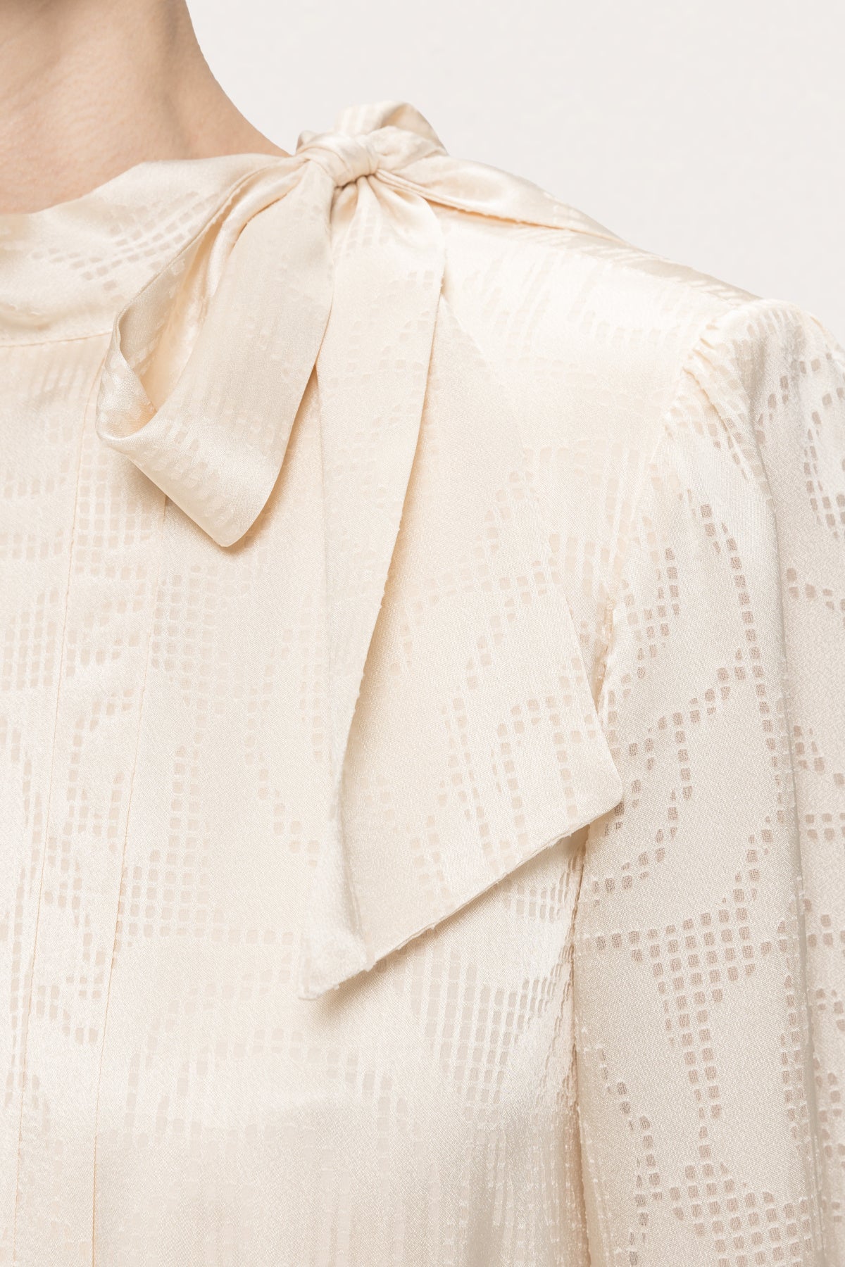Close-up of the shoulder bow and high neckline on NISSA cream satin dress with tonal abstract swirl detailing.