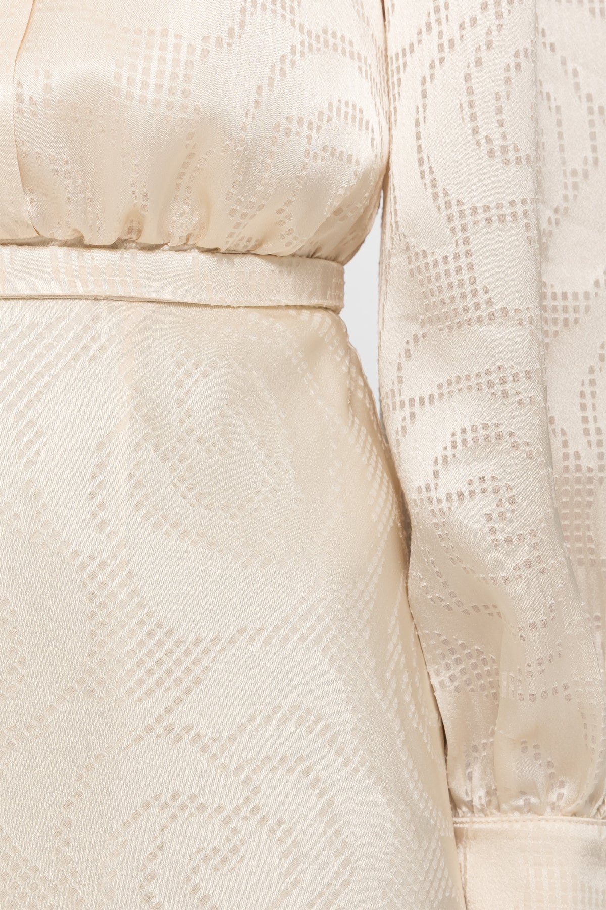 Close-up of NISSA cream satin dress showing tonal swirl motifs, a gathered waist, slim belt and long cuffed sleeve.