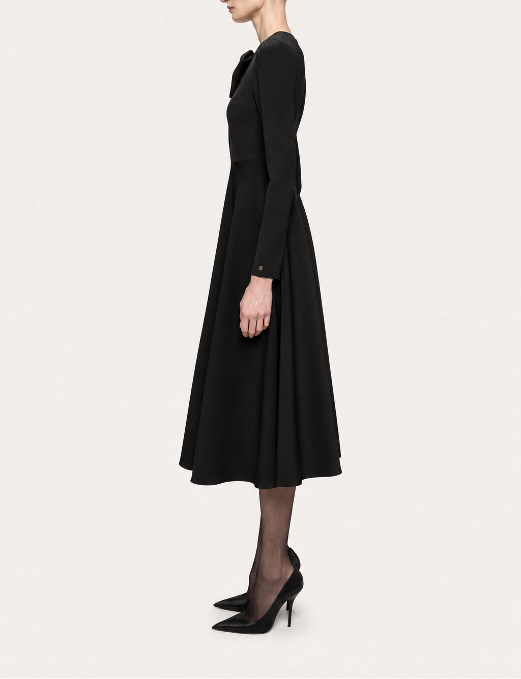 Side view of NISSA black bow-detail midi dress showing the fitted bodice, long sleeve and flared hem.