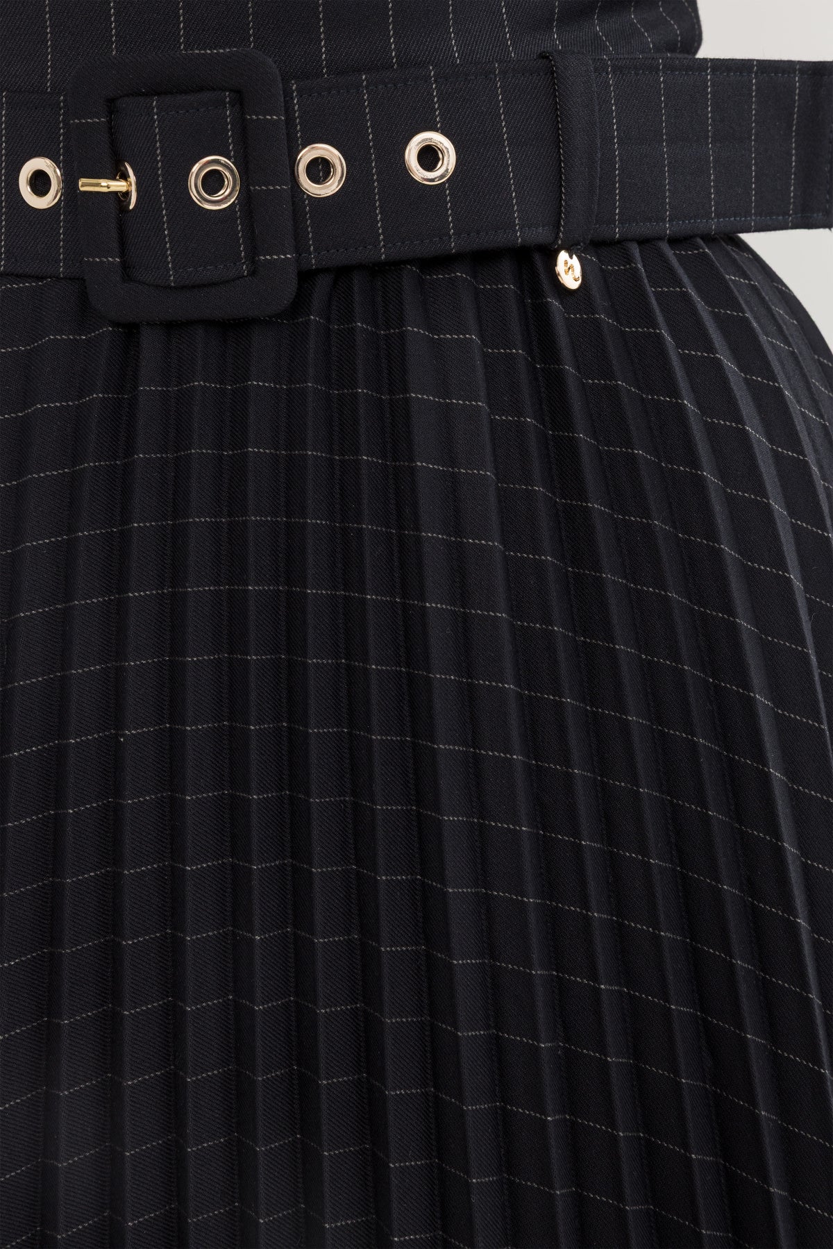 Close-up of black pinstripe midi dress belt with buckle and metal eyelet detail on pleated skirt