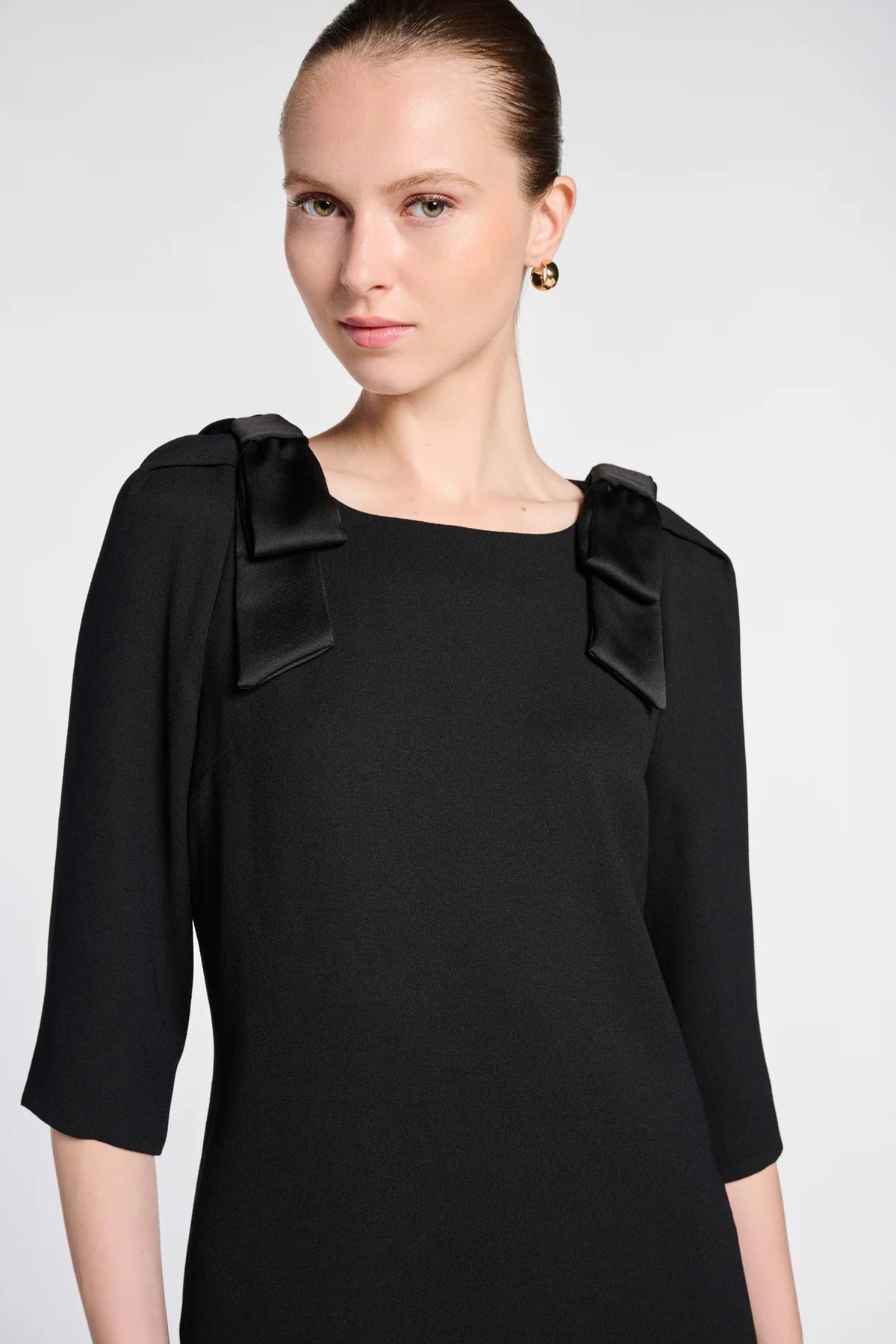 Close-up of satin bows at the shoulders and the round neckline of WEILL Paris black cocktail dress.