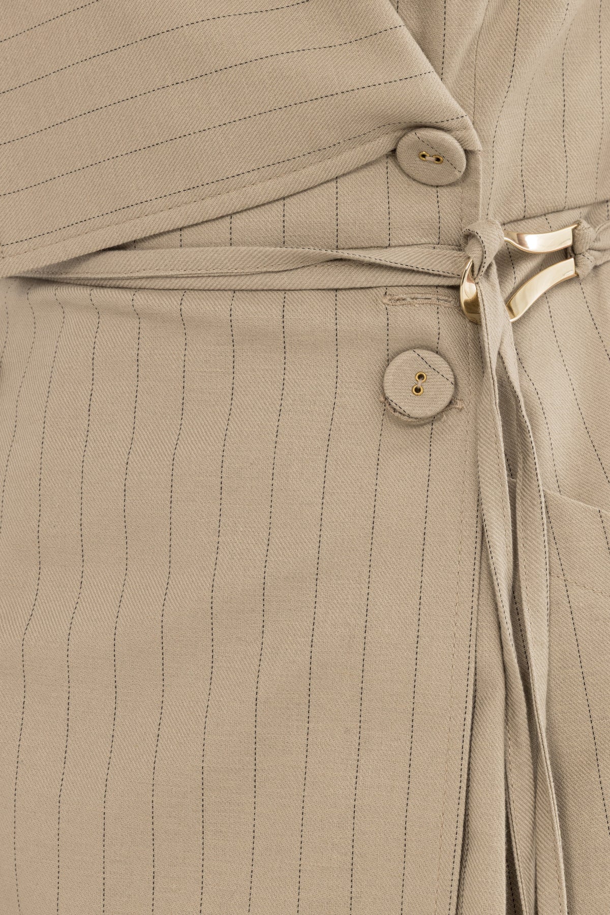 Close-up detail of beige pinstripe fabric, covered buttons, waist tie, and gold hardware