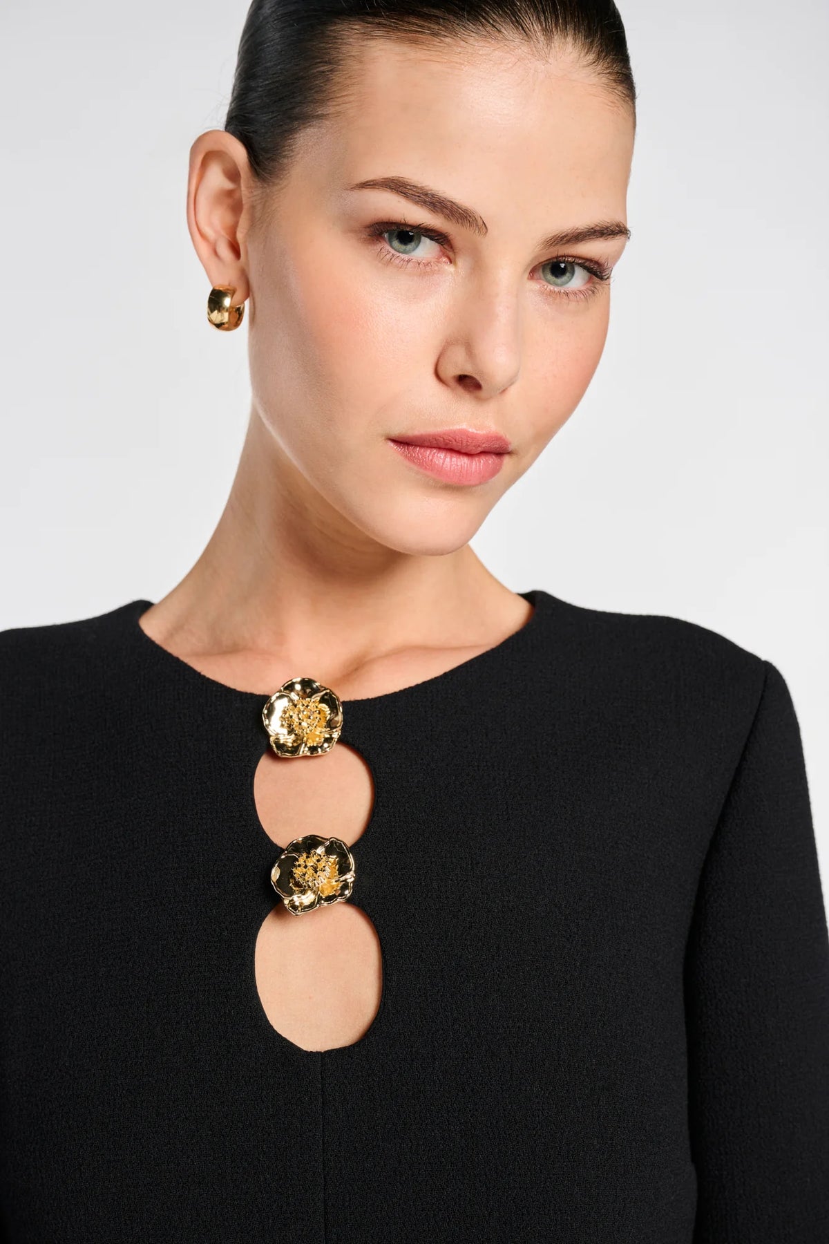Close-up of two gold-tone floral buttons and rounded keyhole openings on a black Weill wool crepe dress.