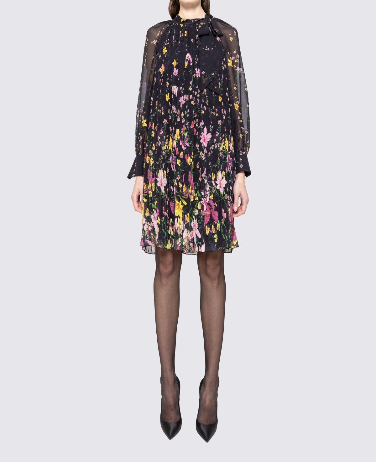 Front view of black floral pleated knee length dress with scarf‑tie bow neck and sheer long sleeves