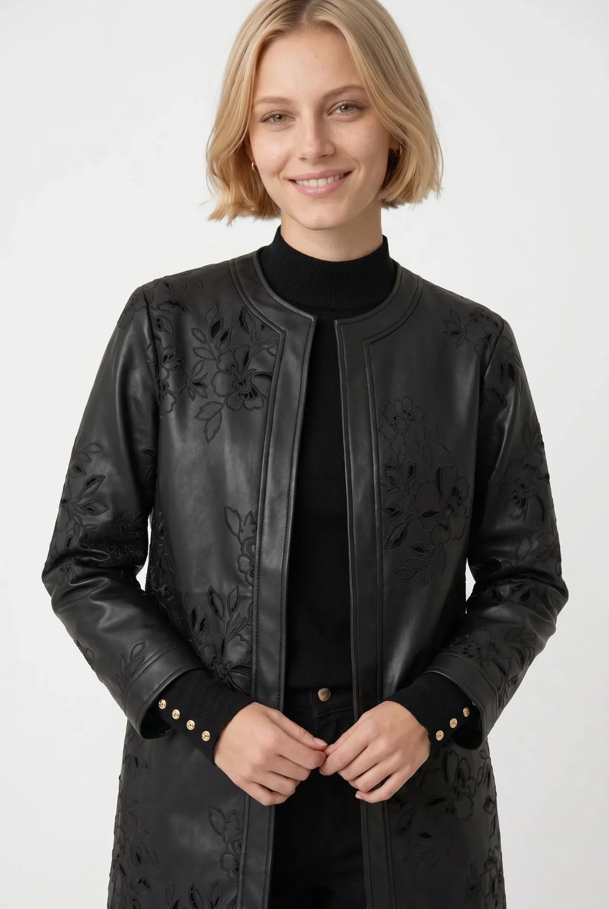 Close-up of tonal floral embroidery and leaf-shaped openwork on a Weill Paris black faux leather coat.