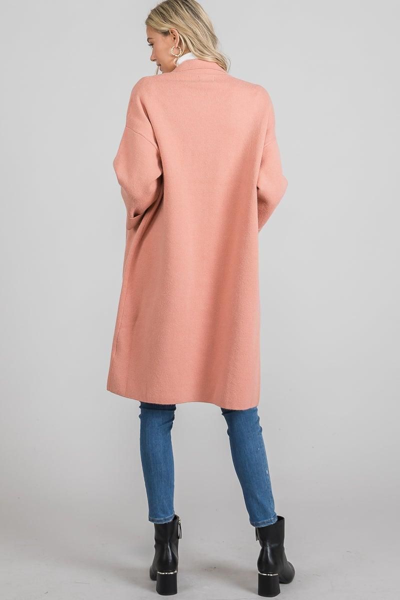 Back view of the mauve longline knit jacket showing dropped shoulders and a plain back, styled with jeans and ankle boots.