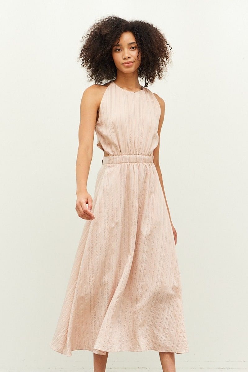 Woman wearing a soft blush-beige halter neck midi dress with tie waist from Grade & Gather