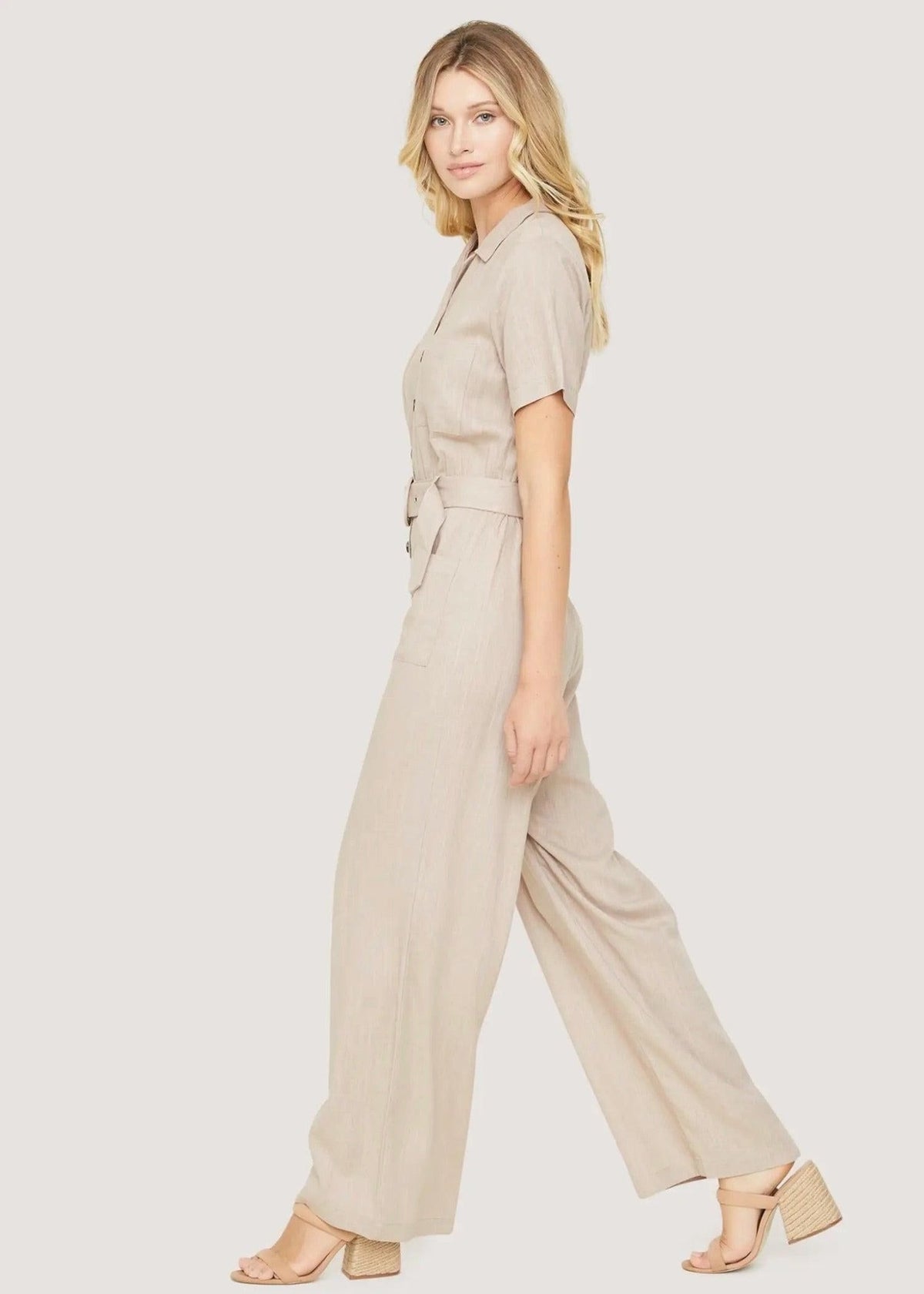Side view of the Weekend Bliss beige wide-leg jumpsuit, styled with neutral block-heel sandals.