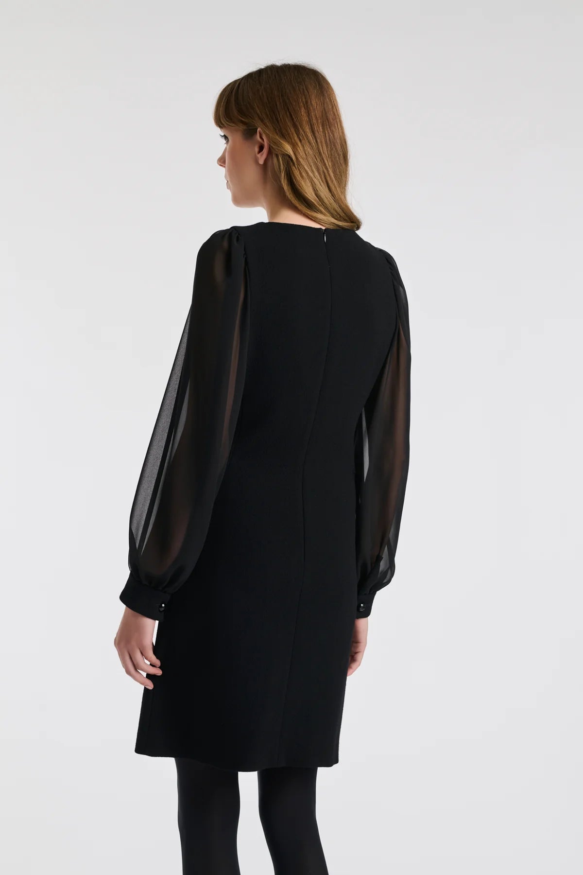 Back three‑quarter: Weill black dress with sheer sleeves, wool crêpe cuffs and concealed back zip.
