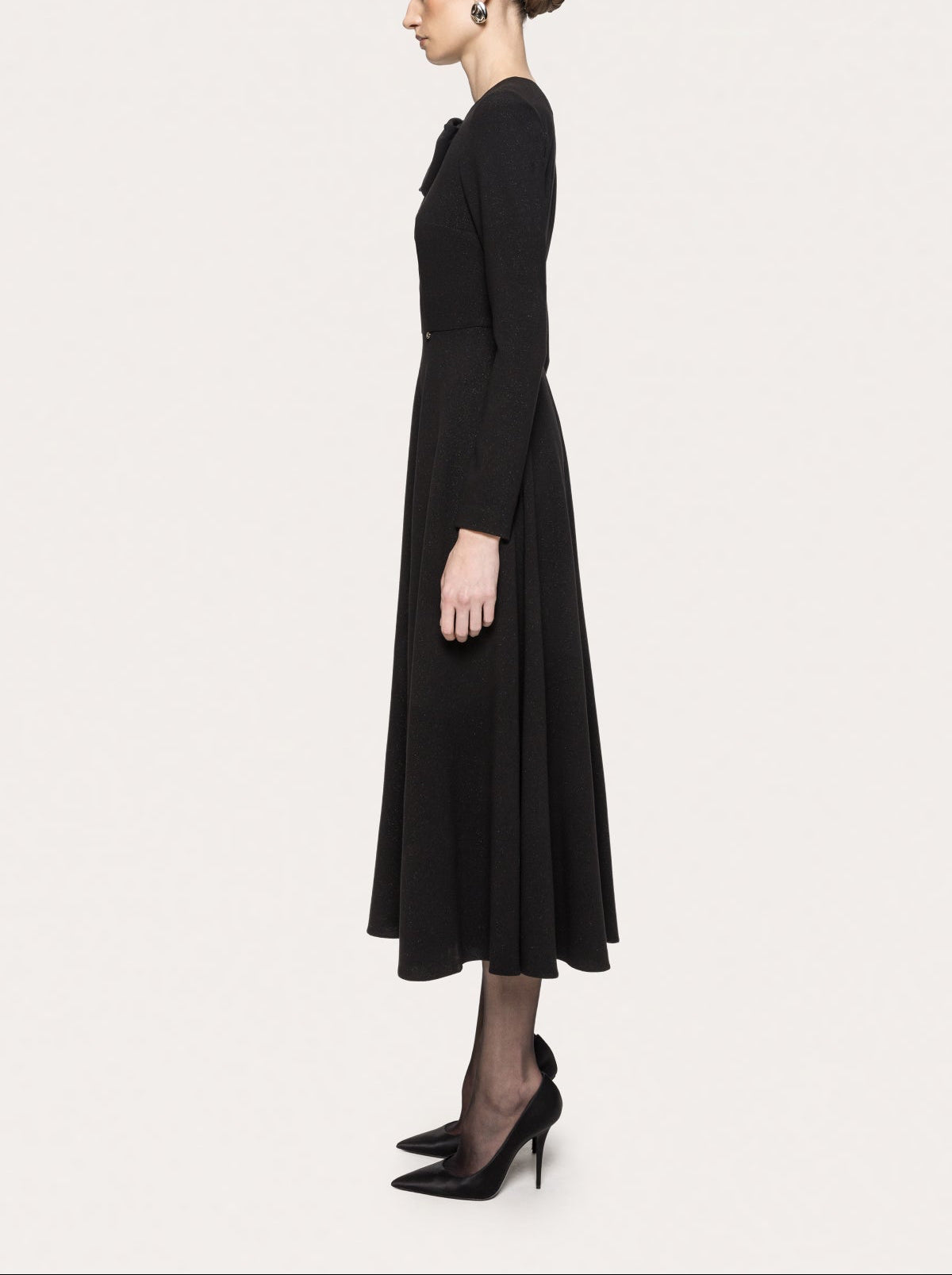 Side view of NISSA black bow midi dress showing the fitted waist, long sleeves and full skirt.