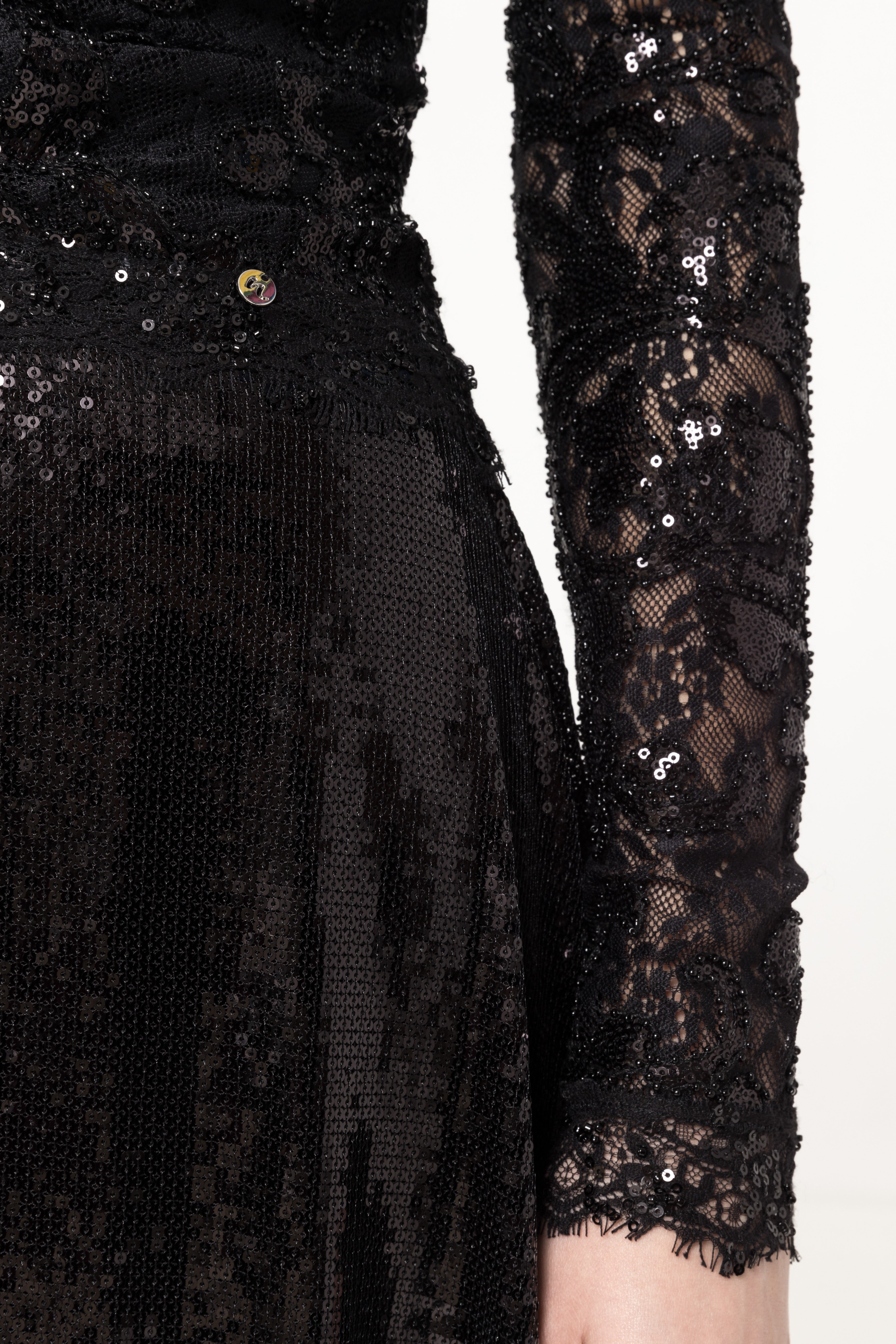 Detail of sequined lace sleeve, waist seam and micro‑sequin A‑line skirt.
