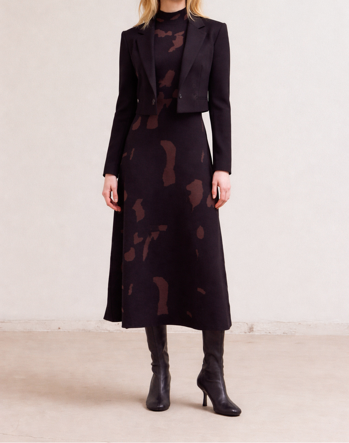 Woman wearing a black fitted knit maxi dress with cropped jacket against a plain background