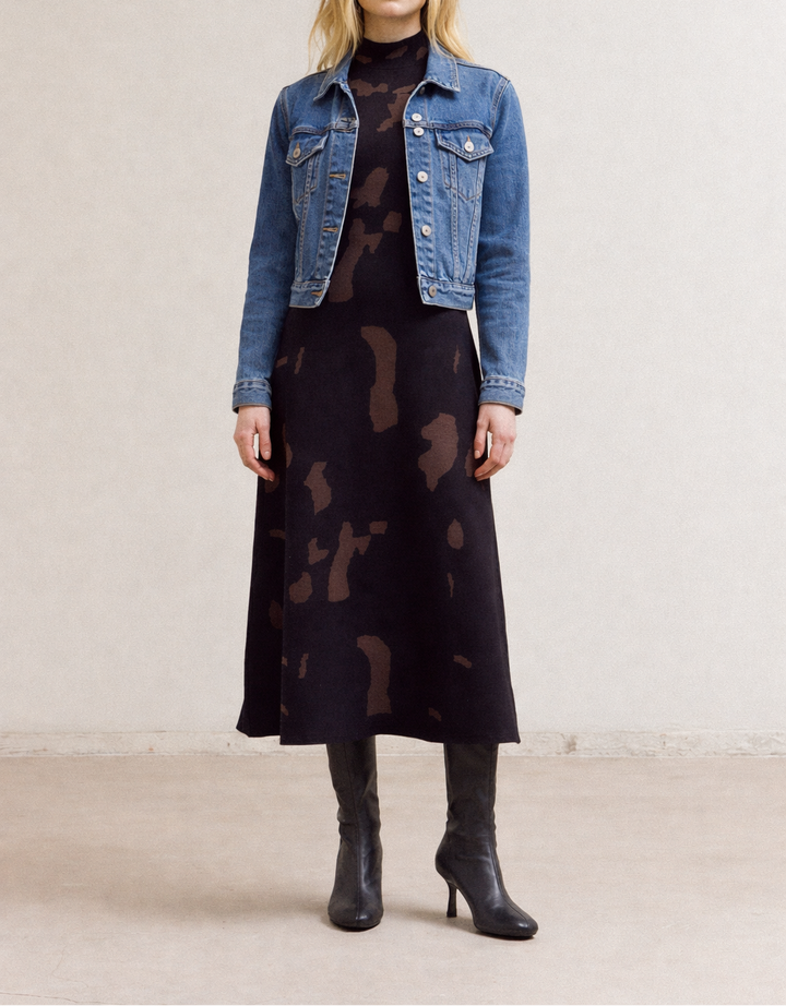 Woman wearing a denim jacket, black Fitted Knit maxi dress, and black boots on a plain background