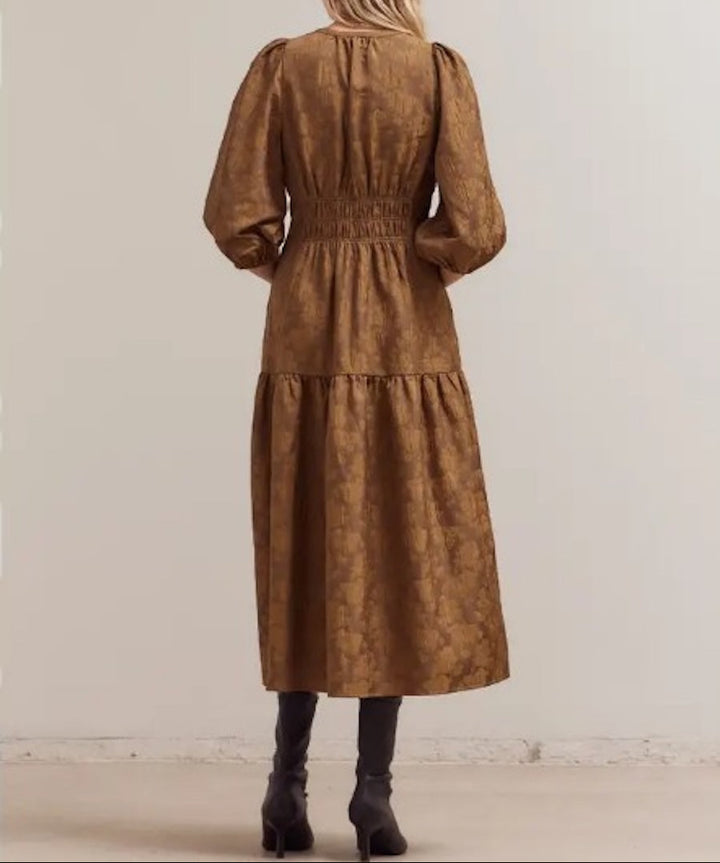 Back view of a cacao floral jacquard midi dress showing 3/4 puff sleeves, a smocked waist, and a softly flared tiered midi skirt, paired with ankle boots.