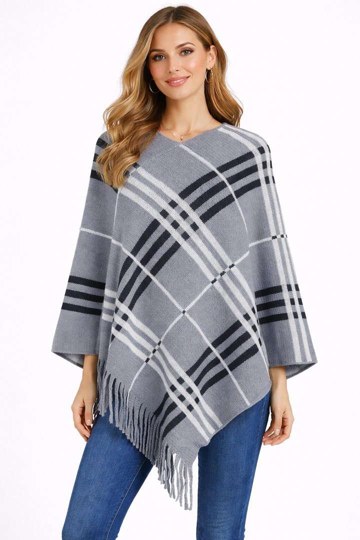 Woman wearing a gray and black plaid poncho with fringe on a white background