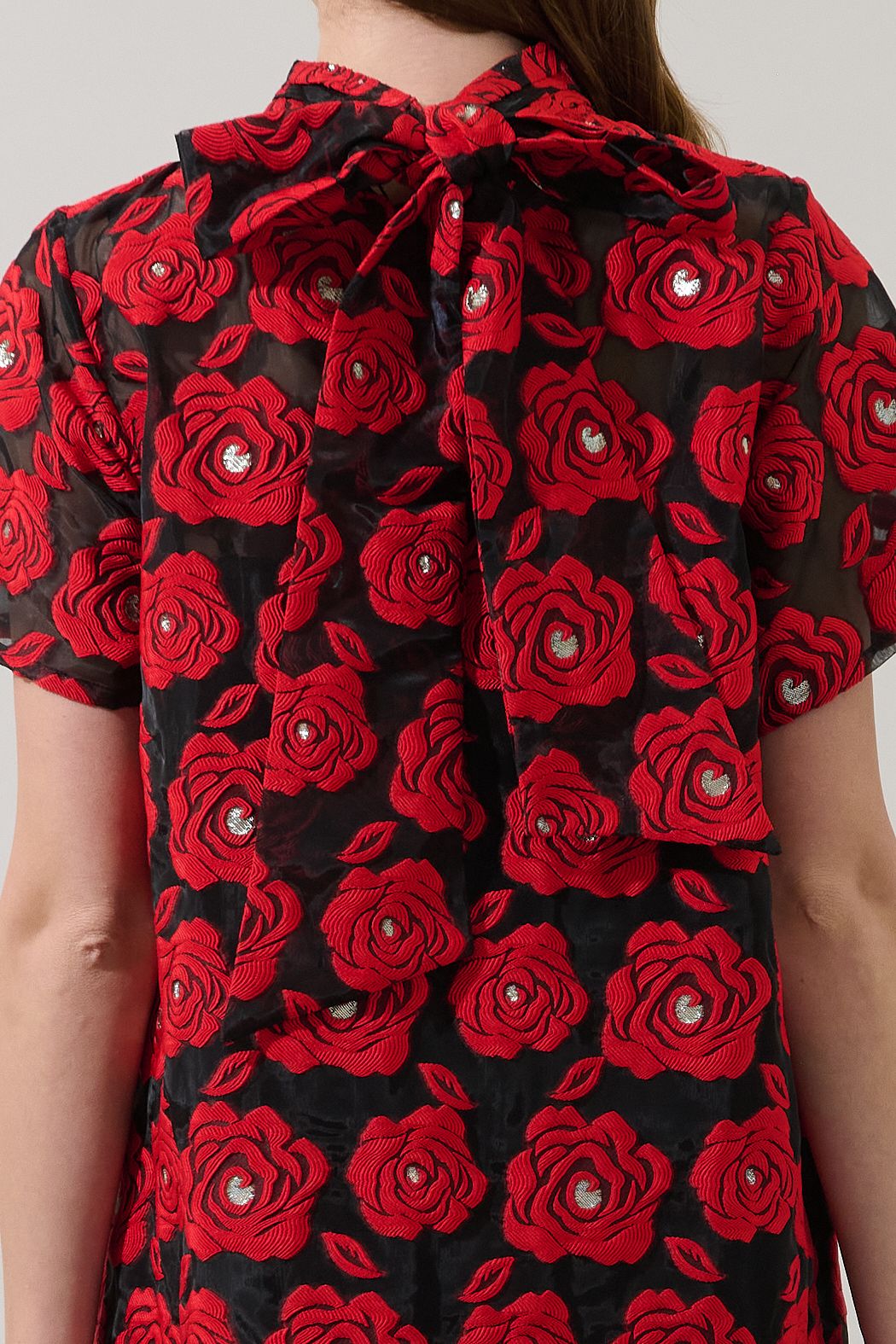 Close-up of the Berny dress back bow, textured red rose pattern and silver-tone accents on black organza