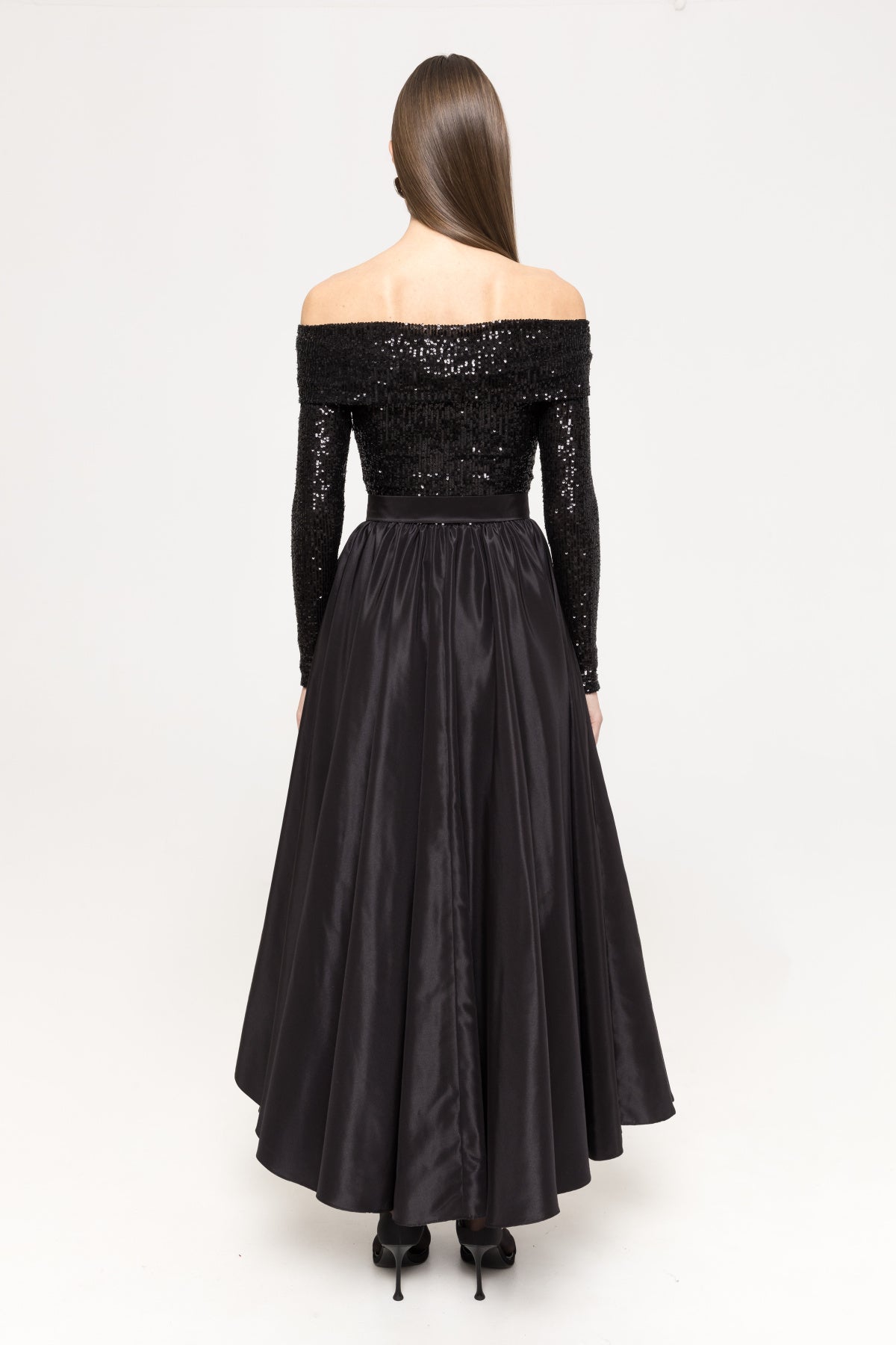 Back view of the black off‑shoulder, long‑sleeve sequin‑panel midi dress featuring an accentuated waist and concealed zipper closure.