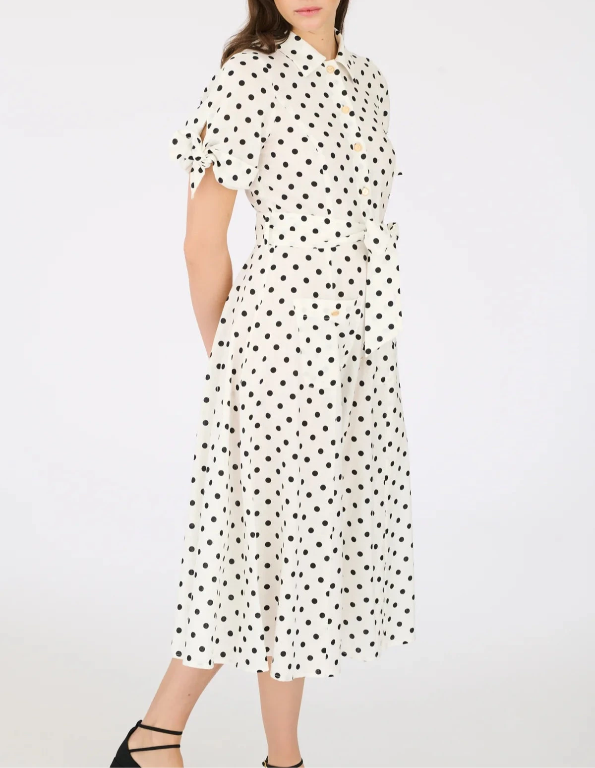 Model wearing white midi polka dot shirt dress with tie sleeves, button-down front, and waist belt