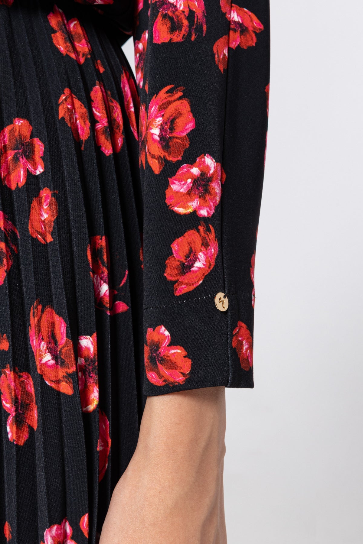 Close‑up of buttoned cuff and pleated skirt in red poppy print on black fabric