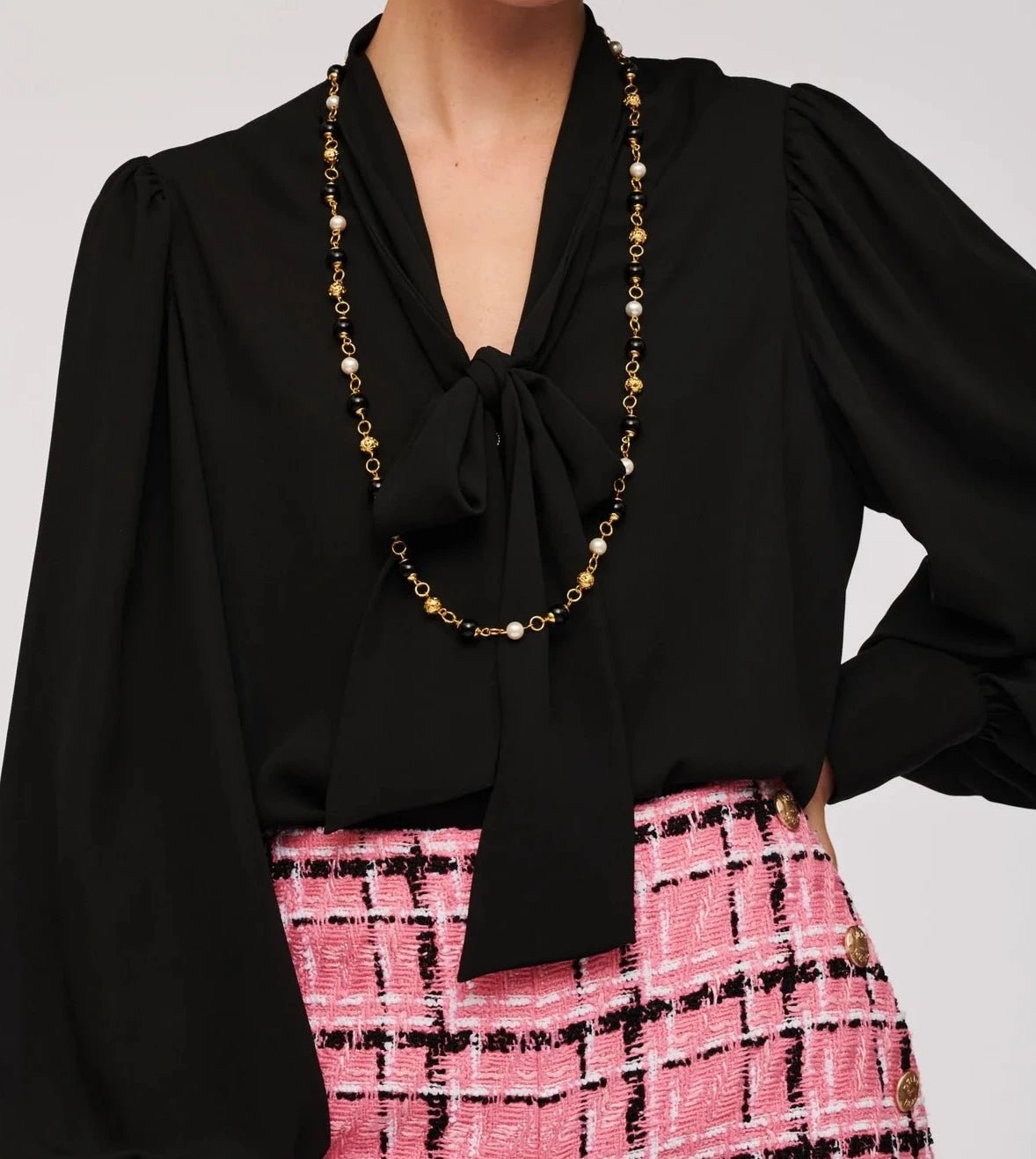 WEILL Paris pearl-look and black bead station necklace styled with a black tie-neck blouse and pink tweed skirt.
