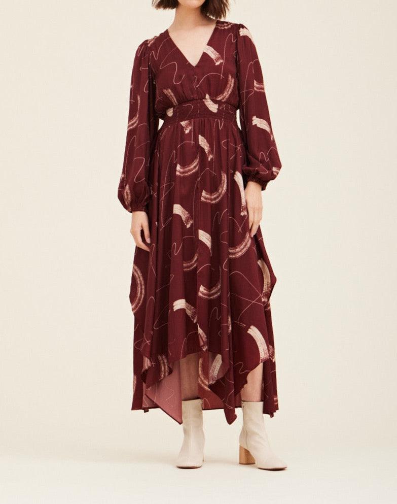 Front view of the Grade & Gather Vino burgundy abstract satin maxi dress with a smocked waist and asymmetrical hem.