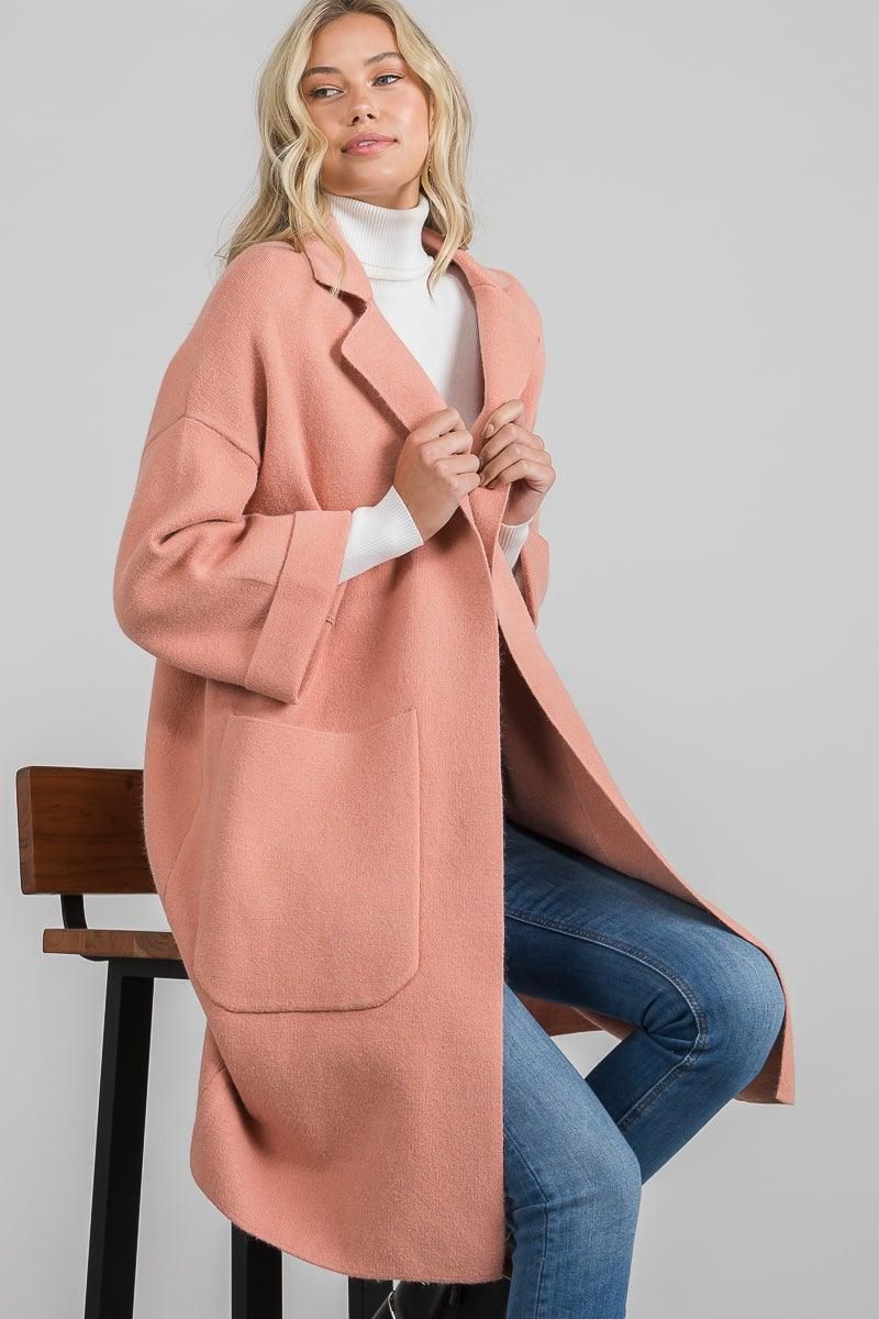 Seated model wearing a mauve open-front knit jacket with notched lapels and large patch pockets over a white turtleneck.