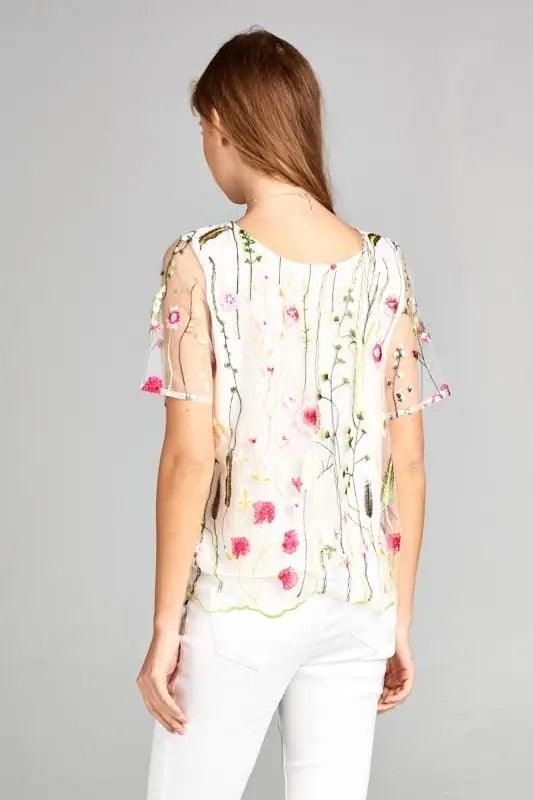 Angled back view of the white floral embroidered top with sheer short sleeves and a lined body.