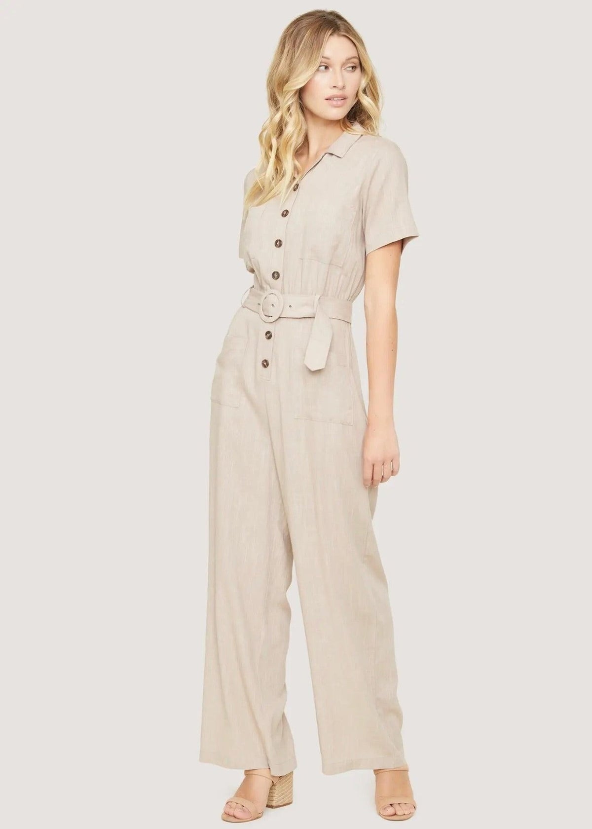 Three-quarter front view of the almond Weekend Bliss jumpsuit showing its shirt collar, belt and front patch pockets.